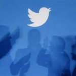 Shadows of people holding mobile phones are cast onto a backdrop projected with the Twitter logo in Warsaw
