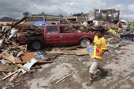 A boy carrying a plastic bottle of water walks past a car which slammed into damaged houses after super Typhoon Haiyan battered Tacloban city
