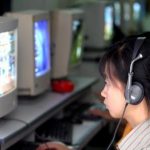 School girl uses headphone while surfing web at public cafe internet in Hanoi