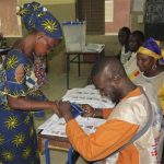 A woman carries a baby on her back as she casts her vote during a legislative vote at a polling station in Lafiabougou, Bamako