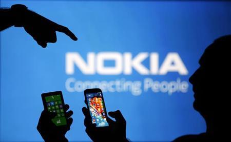 Men are silhouetted against a video screen with a Nokia logo as he poses with Nokia Lumia 820 and Samsung S4 smartphones in this photo illustration taken in the central Bosnian town of Zenica