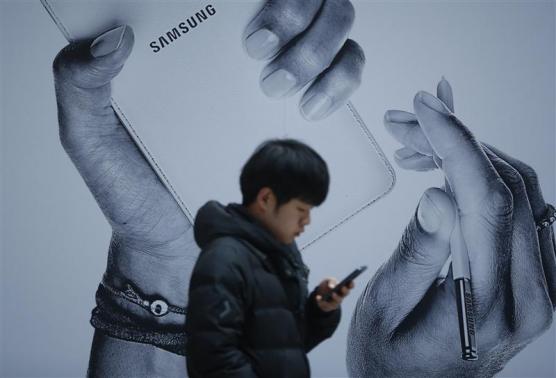 A passenger using his mobile phone walks past an advertisement promoting Samsung Electronics' Galaxy Note 3 at its exhibition hall at a railway station in Seoul