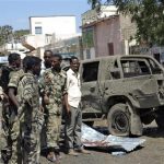 Somali policemen stand next to a damaged car at the scene of an explosion in Baladweyne in central Somalia