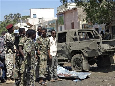 Somali policemen stand next to a damaged car at the scene of an explosion in Baladweyne in central Somalia