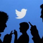 People holding mobile phones are silhouetted against a backdrop projected with the Twitter logo in Warsaw