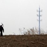 A mobile phone tower is seen behind a man carrying a pick over his shoulder on the outskirts of Beijing