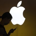 A woman looks at the screen of her mobile phone in front of an Apple logo outside an Apple store in downtown Shanghai