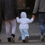 A girl holds the hands of her parents as they walk on a street in Beijing