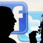 Man uses tablet computer while standing in front of video screen with Facebook and Twitter logos in this picture illustration taken in Sarajevo
