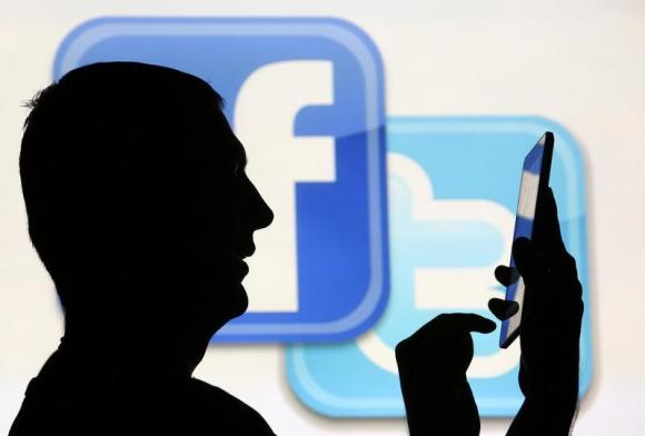 Man uses tablet computer while standing in front of video screen with Facebook and Twitter logos in this picture illustration taken in Sarajevo