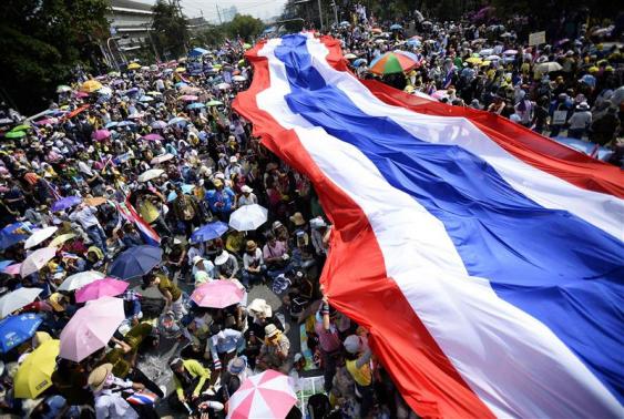 Anti-government protesters unveil a large Thai flag as they descend on Government House in Bangkok