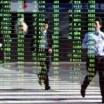 Pedestrians are reflected on a stock quotation board at a brokerage in Tokyo