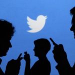 People holding mobile phones are silhouetted against a backdrop projected with the Twitter logo in Warsaw