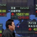 A pedestrian walks past an electronic board displaying various countries' share prices outside a brokerage in Tokyo