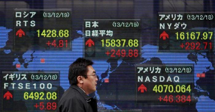 A pedestrian walks past an electronic board displaying various countries' share prices outside a brokerage in Tokyo