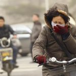 A woman wearing a mask rides her bicycle along a street on a hazy morning in Beijing