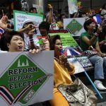 Anti-government protesters blow whistles and hold placards during a rally at Silom road in central Bangkok