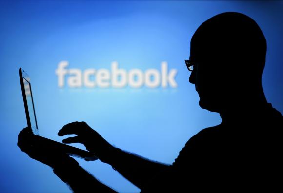 A man is silhouetted against a video screen with an Facebook logo as he poses with an Dell laptop in this photo illustration taken in the central Bosnian town of Zenica