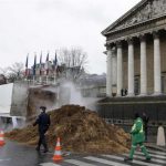 French police and municipal workers walk near a large pile of manure sitting in front of the National Assembly in Paris