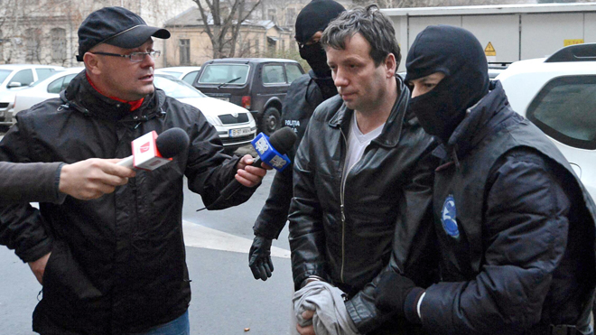 Lehel, alleged hacker "Guccifer", is escorted by masked policemen in Bucharest, after being arrested in Arad