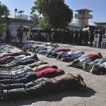 Inmates lie on the ground as riot policemen keep watch after a gunfight at the Tuxpan prison in Iguala
