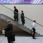 People walk past an electronic information board at the London Stock Exchange in the City of London