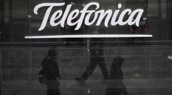 People are reflected as they walk past Spanish telecom group Telefonica's flagship store in central Madrid