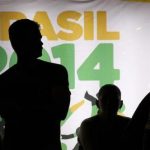People are silhouetted in front of an advertisement of the Brazil 2014 FIFA Soccer World Cup as they wait for a bus in Recife