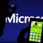 Photo illustration shows a man silhouetted against a video screen with the Microsoft logo in the background as he poses with a Nokia Lumia 820 smartphone in Zenica