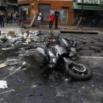 A protester throws stones at a motorcycle after the rider tried to past a barricade in Caracas