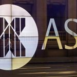An office worker walks past the board of the Australian Securities Exchange building displaying its logo in central Sydney