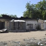 Women walk by homes destroyed by Boko Haram militants in Bama