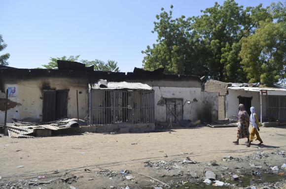 Women walk by homes destroyed by Boko Haram militants in Bama