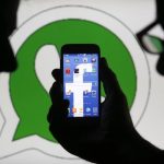 An illustration photo shows a man holding a smart phone with a Facebook logo as its screen wallpaper in front of a WhatsApp messenger logo, in Zenica
