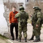 Armed men, believed to be Russian servicemen, stand guard and talk with a local man outside an Ukrainian military base in Perevalnoye