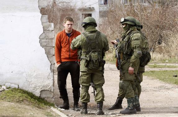 Armed men, believed to be Russian servicemen, stand guard and talk with a local man outside an Ukrainian military base in Perevalnoye