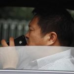 A man uses his iPhone as he drives a car along a main road in central Beijing