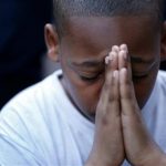 A young boy folds his hands in prayer
