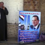 Shehata, a supporter of Egypt's former president Mubarak drinks tea as he holds poster, outside police academy, where Mubarak's trial will take place, in Cairo