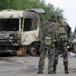 Pro-Russian separatists stand guard at a checkpoint near a burnt truck outside Luhansk