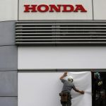 Workers stand under the logo of Honda Motor Co. outside the company's headquarters in Tokyo