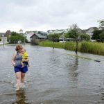 Vacationer Cornwell of Tennessee carries her eight-month-old son Riley, through a flooded street after Hurricane Arthur passed through in Manteo