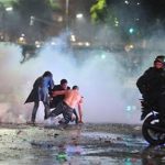 Soccer fans try to escape from a tear gas cloud and a police water cannon