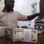 A money dealer counts the Nigerian naira on a machine in his office in the commercial capital of Lagos