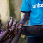 A social mobilizer from NGO (AJCOM), carries a basin of water past the soapy hands of children, to help prevent the spread Ebola in Conakry