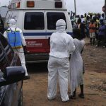 Health workers bring woman suspected of having contracted Ebola virus to an ambulance in front of a crowd in Monrovia