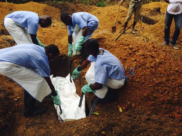 Volunteers lower a corpse, which is prepared with safe burial practices, into a grave in Kailahun