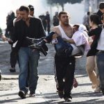 Injured Kurdish protester is carried by his friend as they clash with riot police in Diyarbakir