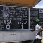 Bystanders read headlines saying "Ebola 1: USA 0" at the Daily Talk, a street side chalkboard newspaper, in Monrovia
