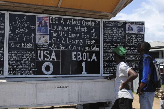Bystanders read headlines saying "Ebola 1: USA 0" at the Daily Talk, a street side chalkboard newspaper, in Monrovia